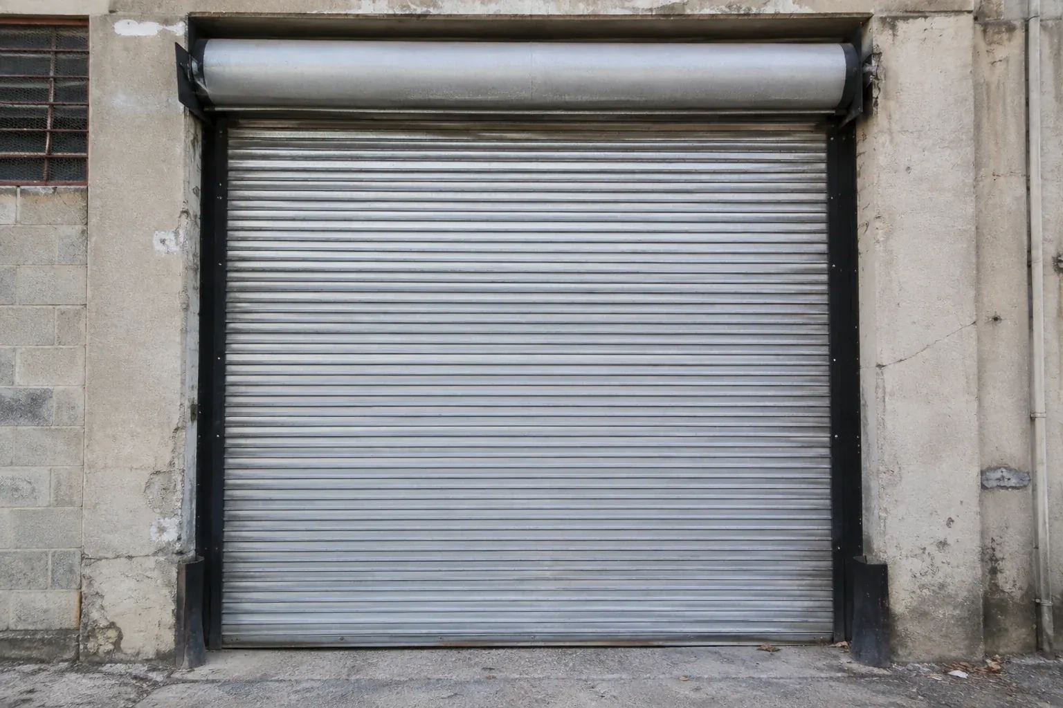 Closed metal rolling shutter in a weathered warehouse opening. — Commercial Rolling Door Repair, Waterloo