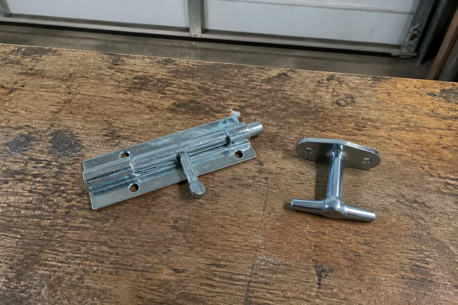 Detached slide bolt and T-handle on a wooden garage workbench. — Garage Door Manual Lock Repair, Waterloo